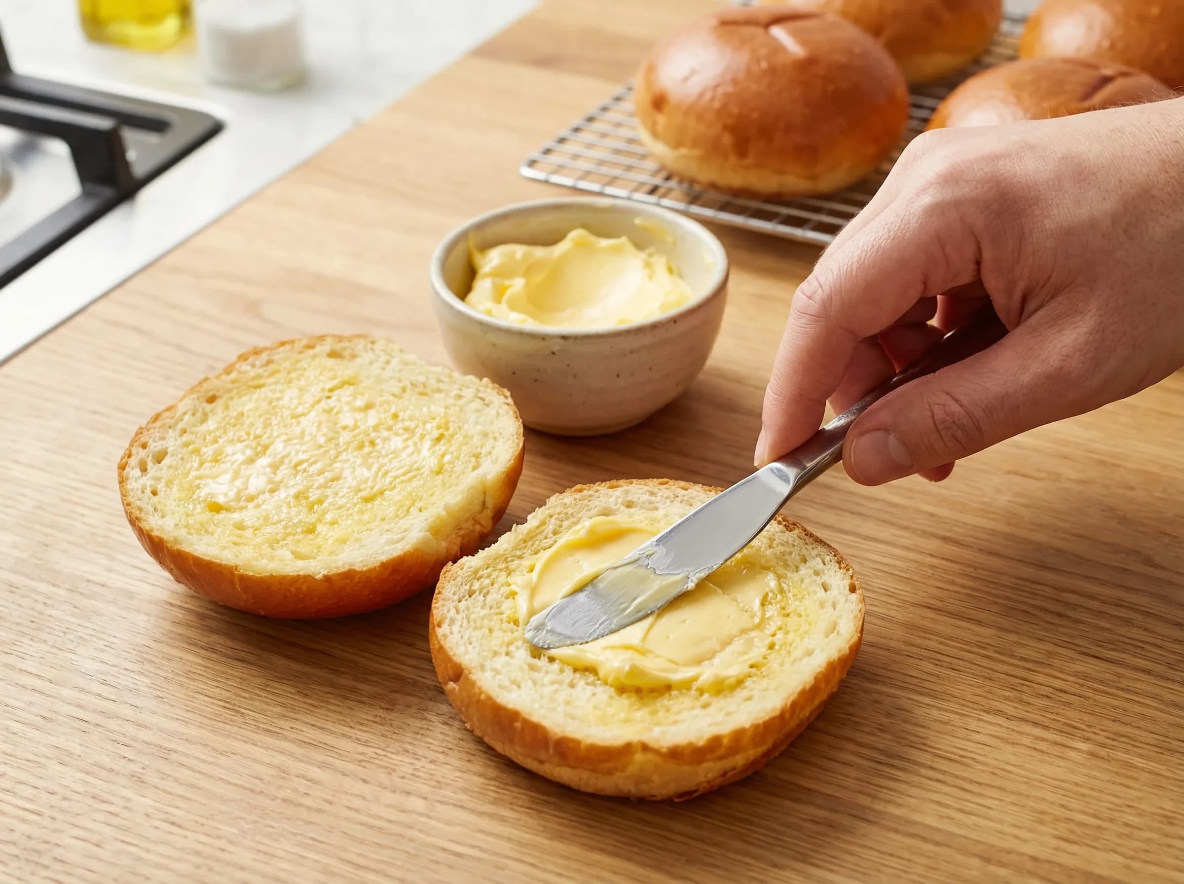 Melted butter being spread on cut burger bun surfaces